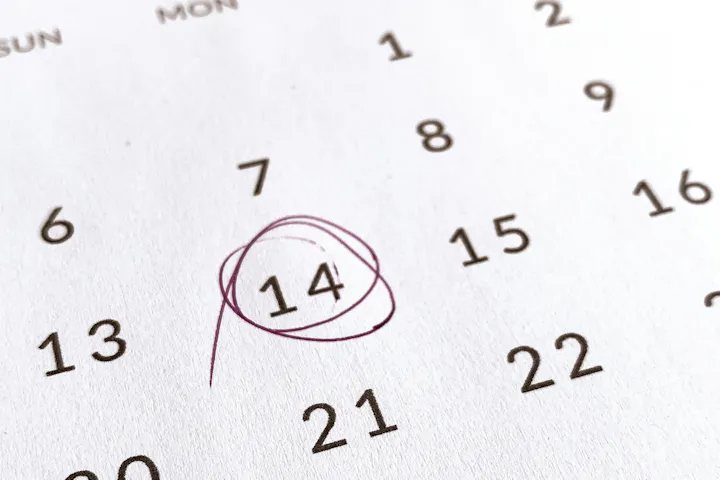 Close-up of a paper calendar with the 14th circled in pen