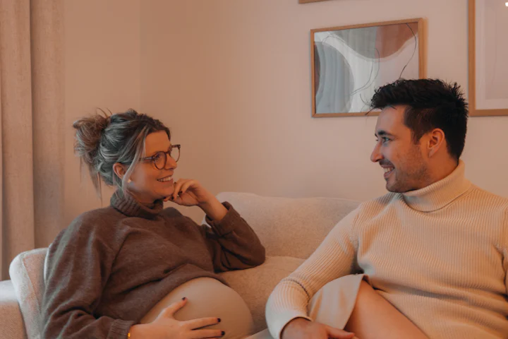 Expecting couple sitting on a sofa at home, smiling at each other