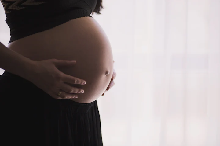 Pregnant woman cradling her bump with both hands beside a bright window